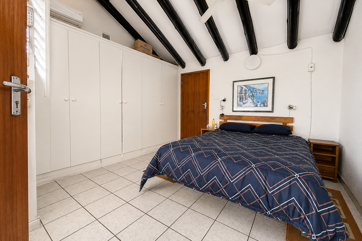 A well-maintained bedroom featuring exposed ceiling beams, built-in cupboards, tiled flooring, and a split-system air conditioner for climate control.