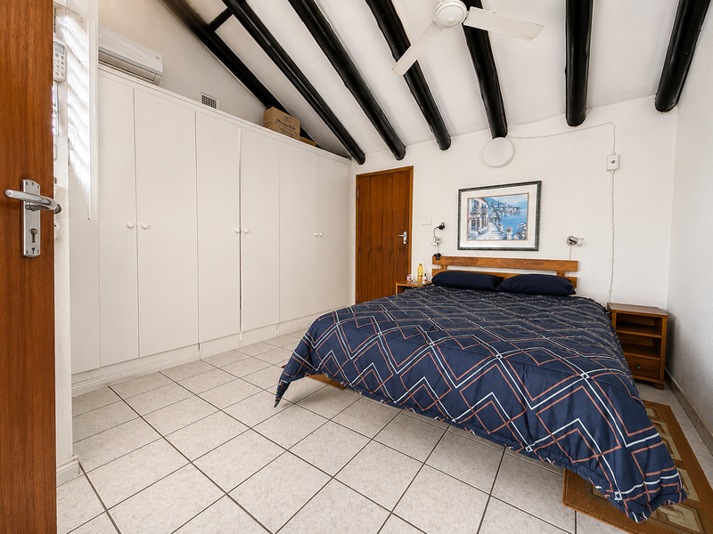 A well-maintained bedroom featuring exposed ceiling beams, built-in cupboards, tiled flooring, and a split-system air conditioner for climate control.
