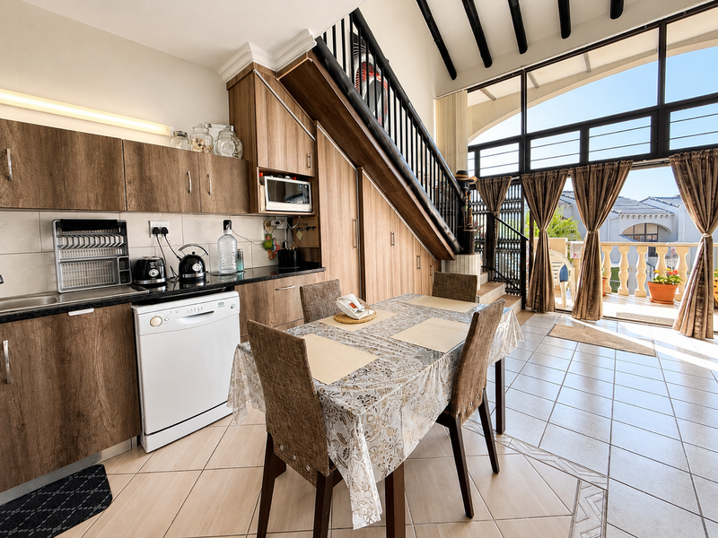 Open-plan kitchen and dining area featuring wood-finish cabinetry, built-in appliances, tiled flooring, and a staircase leading to an upper level with balcony access.