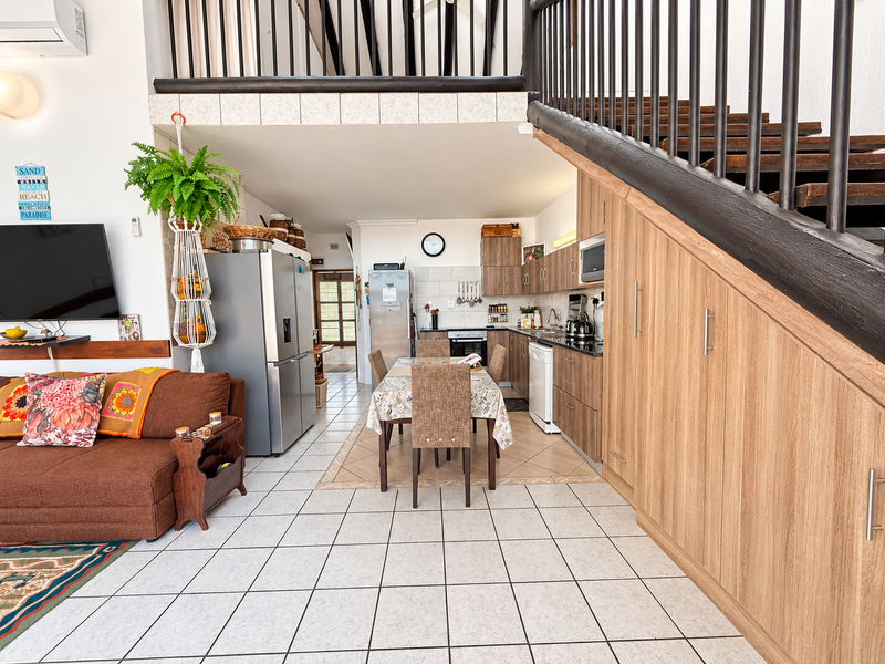 Open-plan living and kitchen area featuring tiled floors, modern wood-finish cabinetry, integrated appliances, and a staircase leading to an upper level.