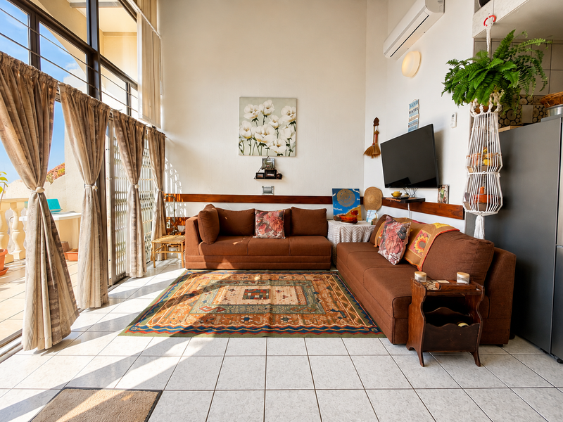 Bright living room featuring large floor-to-ceiling windows, tiled flooring, and a wall-mounted air conditioning unit, with direct access to an outdoor balcony area.