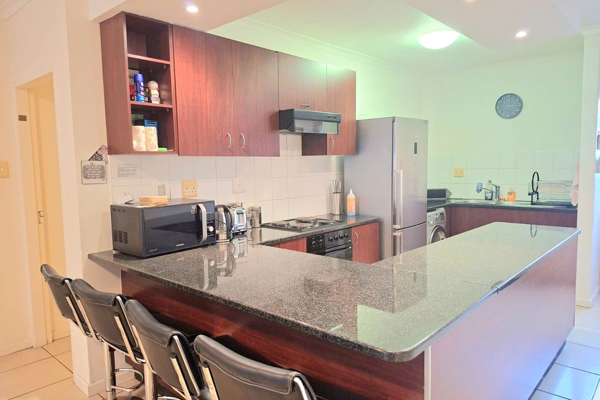 A functional kitchen featuring dark wood cabinetry, granite countertops, a breakfast bar, and integrated appliances, finished with tiled flooring and recessed lighting.