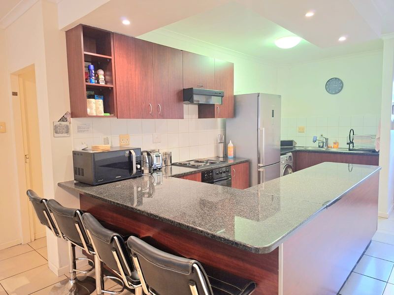 A functional kitchen featuring dark wood cabinetry, granite countertops, a breakfast bar, and integrated appliances, finished with tiled flooring and recessed lighting.