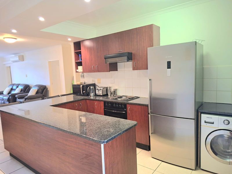 Open-plan kitchen featuring granite countertops, dark wood-finish cabinetry, integrated appliances, and tiled flooring, seamlessly flowing into the adjacent living area.
