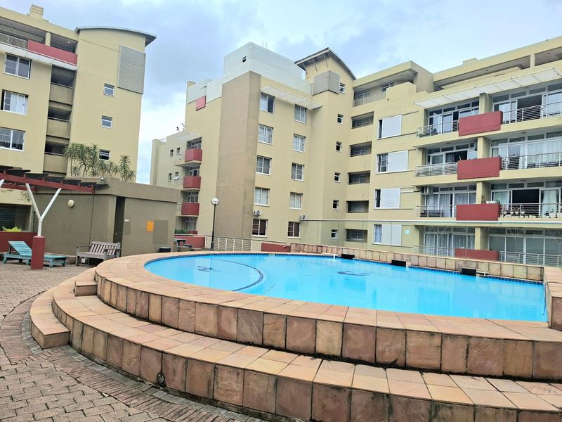 Communal swimming pool area featuring a raised tiled surround, paved patio space, and views of the surrounding apartment building facades.