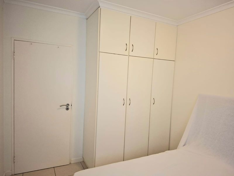 A bedroom featuring a floor-to-ceiling built-in wardrobe with white cabinetry and neutral finishes.