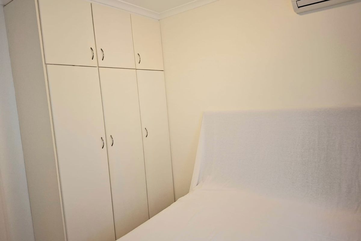 A bedroom featuring built-in cabinetry for storage and a wall-mounted split-system air conditioning unit.