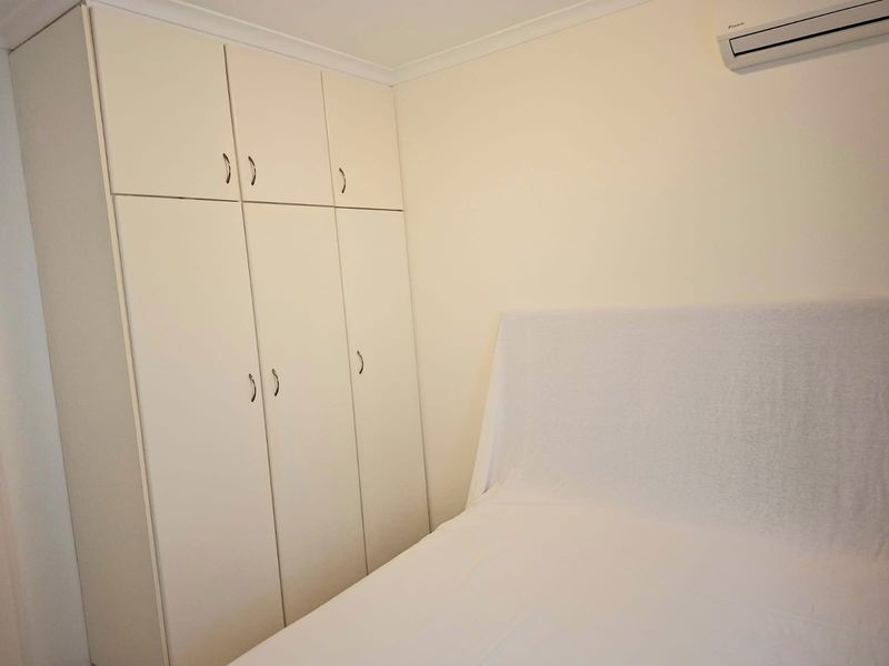 A bedroom featuring built-in cabinetry for storage and a wall-mounted split-system air conditioning unit.