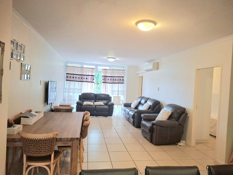Spacious open-plan living and dining area featuring neutral tiled flooring, a wall-mounted air conditioning unit, and access to an outdoor space via sliding doors.