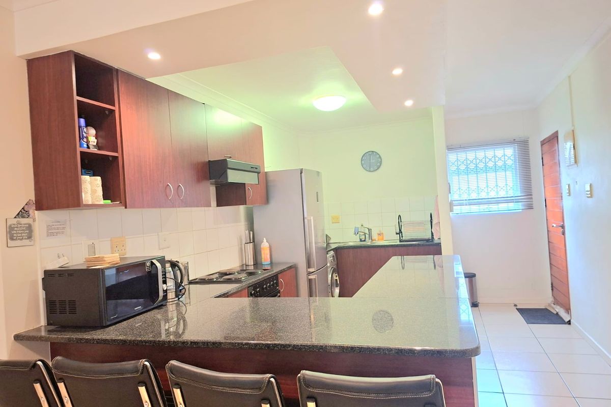 Functional kitchen featuring dark wood cabinetry, granite countertops, a breakfast bar, and tiled flooring, with an integrated hob and extractor fan.