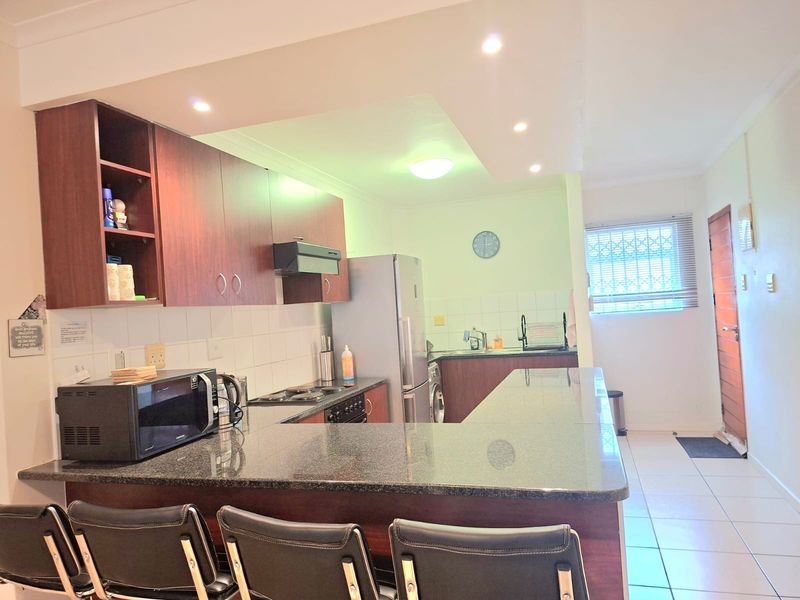 Functional kitchen featuring dark wood cabinetry, granite countertops, a breakfast bar, and tiled flooring, with an integrated hob and extractor fan.