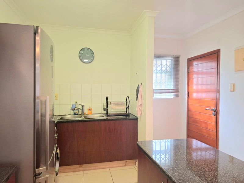 A functional kitchen area featuring dark wood cabinetry, granite countertops, a double sink, and a tiled backsplash, with a wooden door leading to another room.