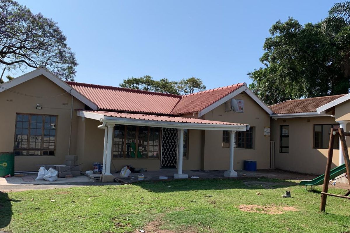 Rear view of a single-story house featuring a covered patio area, corrugated metal roofing, and a spacious garden.