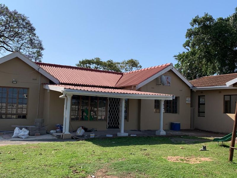 Rear view of a single-story house featuring a covered patio area, corrugated metal roofing, and a spacious garden.