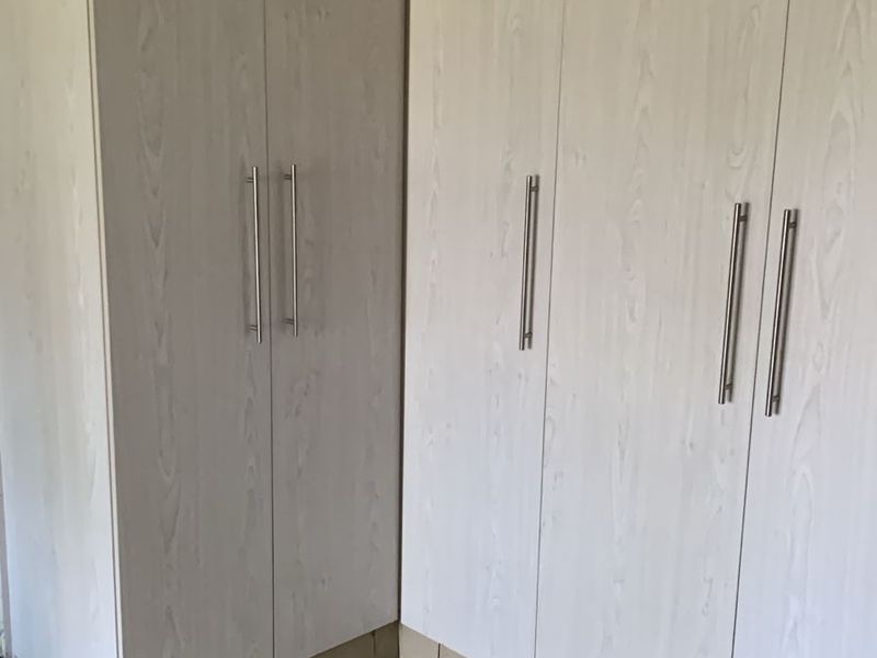 A clean bedroom space featuring light wood-grain built-in cupboards and neutral tiled flooring, offering ample storage and a bright, modern aesthetic.