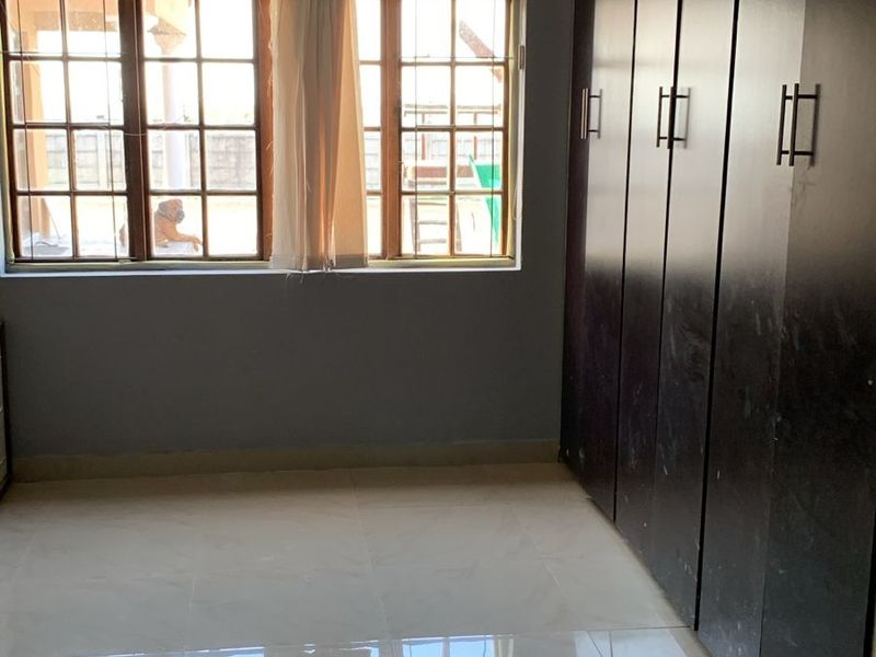 A vacant bedroom featuring tiled flooring, large built-in cupboards, and wooden window frames, showing signs of minor ceiling water staining.