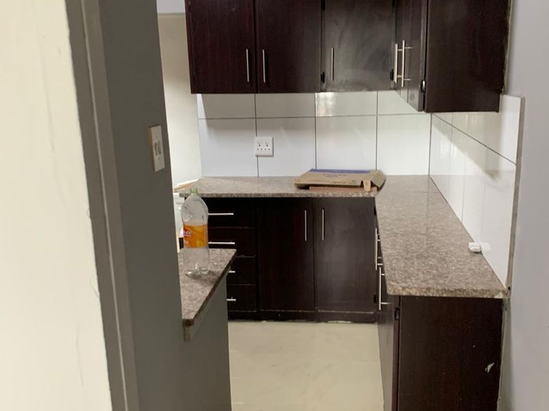 A compact kitchen featuring dark wood-finish cabinetry, laminate countertops, and a tiled backsplash, currently in need of finishing touches to the flooring.
