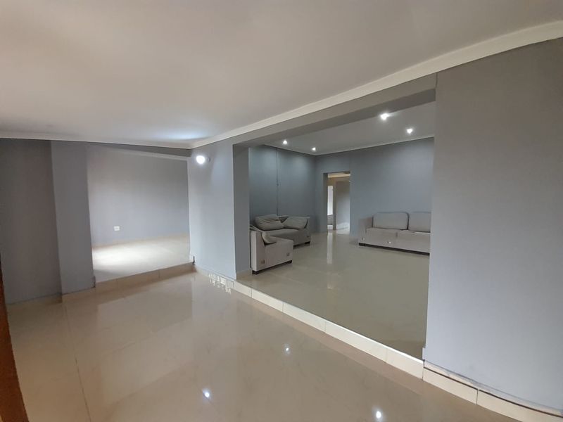 Spacious open-plan living area featuring neutral grey walls, polished tiled flooring, and recessed downlighting throughout the interconnected rooms.