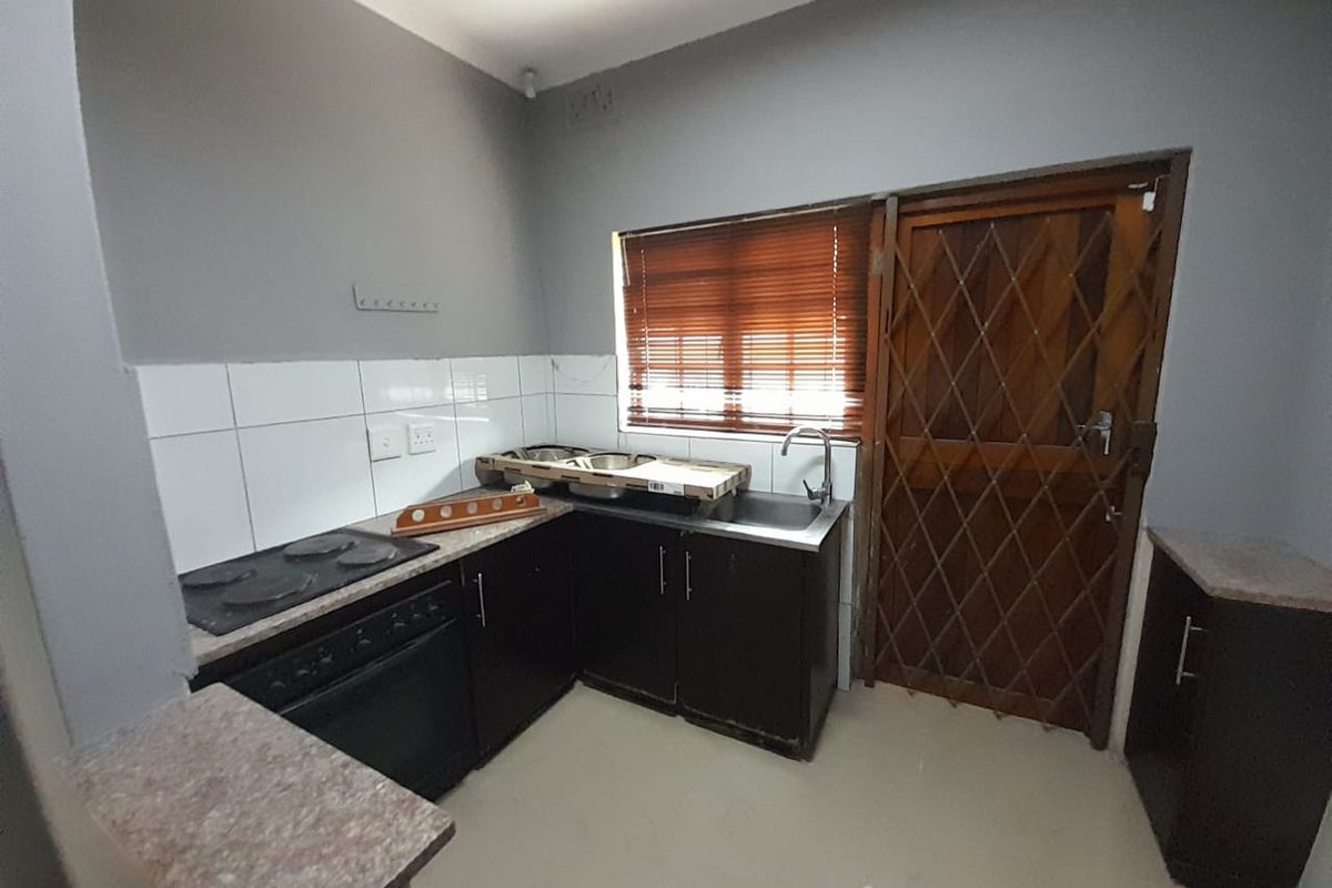A functional kitchen featuring dark cabinetry, laminate countertops, a built-in oven and hob, and a tiled splashback with direct access to the exterior.