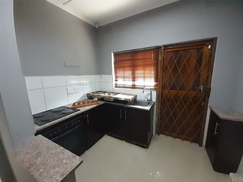 A functional kitchen featuring dark cabinetry, laminate countertops, a built-in oven and hob, and a tiled splashback with direct access to the exterior.