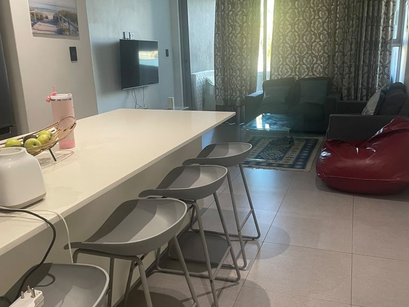 Open plan living area featuring a kitchen island with breakfast bar seating, tiled flooring, and direct access to a balcony through sliding glass doors.