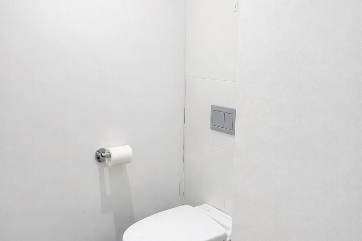 A clean, minimalist bathroom featuring a modern wall-mounted toilet with a dual-flush system and neutral floor tiling.