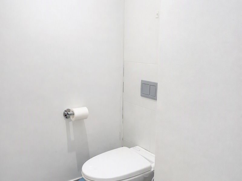 A clean, minimalist bathroom featuring a modern wall-mounted toilet with a dual-flush system and neutral floor tiling.