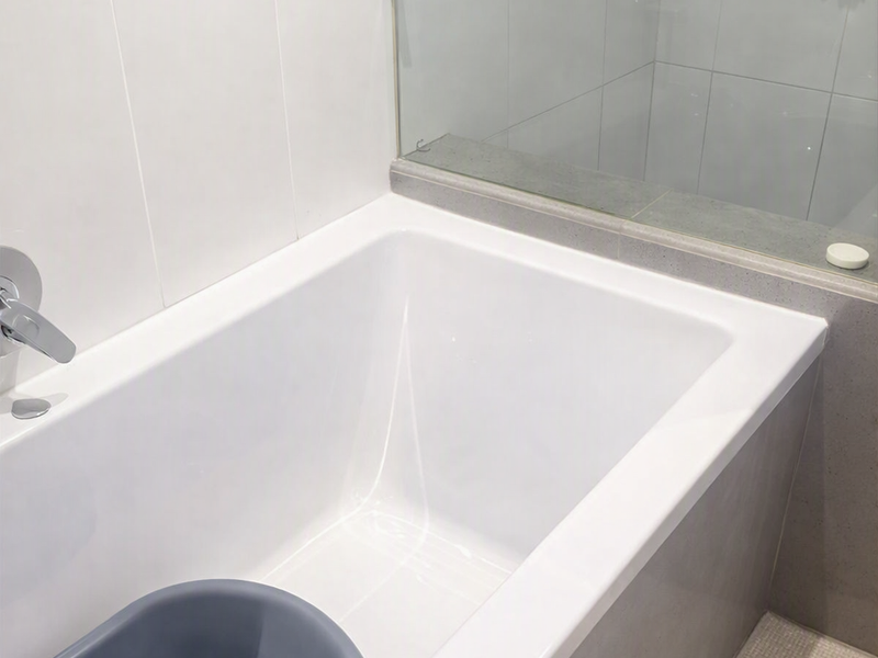 A modern bathroom featuring a clean built-in bathtub with a glass shower screen and neutral wall and floor tiling.