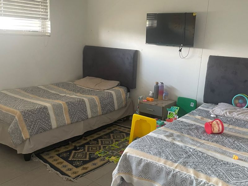 A functional bedroom featuring tiled flooring, venetian blinds, and a wall-mounted air conditioning unit.