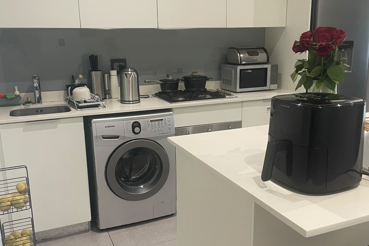 Modern kitchen featuring white cabinetry, stone countertops, integrated washing machine, gas hob, and sleek glass splashback in a clean, functional layout.