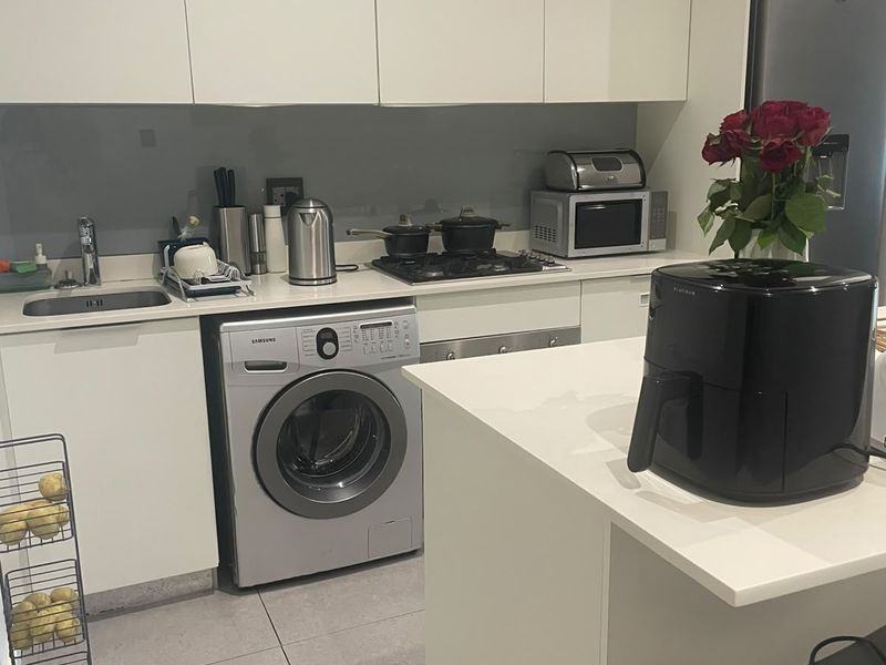 Modern kitchen featuring white cabinetry, stone countertops, integrated washing machine, gas hob, and sleek glass splashback in a clean, functional layout.