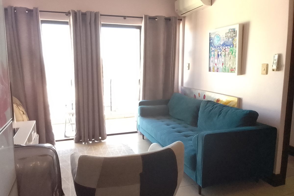 A comfortable living room featuring tiled flooring, a wall-mounted air conditioning unit, and large sliding glass doors providing access to the balcony.