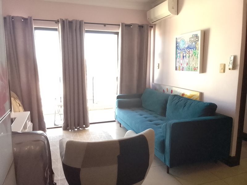 A comfortable living room featuring tiled flooring, a wall-mounted air conditioning unit, and large sliding glass doors providing access to the balcony.