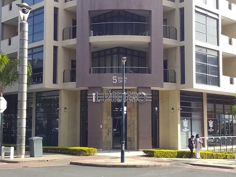 Front elevation of the Il Palizzo apartment building, featuring a modern glass facade, balconies, and professional landscaping at the entrance.