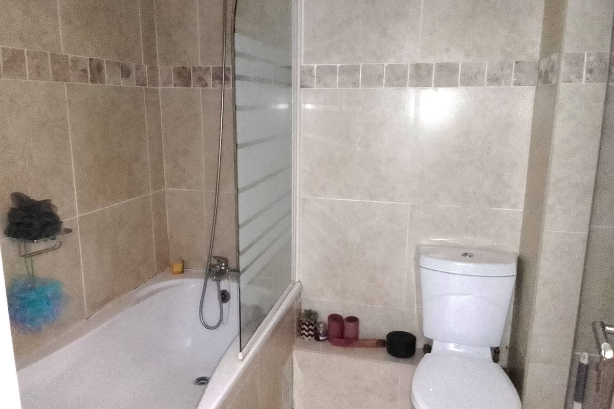 A functional bathroom featuring a bathtub with a glass shower screen, tiled walls, and a standard toilet.