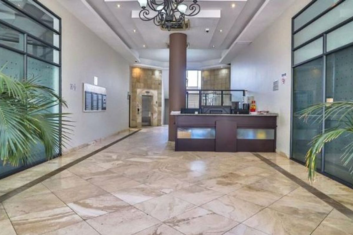 A spacious apartment building lobby featuring a reception desk, tiled flooring, elevator access, and modern glass partition walls.