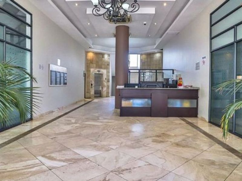 A spacious apartment building lobby featuring a reception desk, tiled flooring, elevator access, and modern glass partition walls.