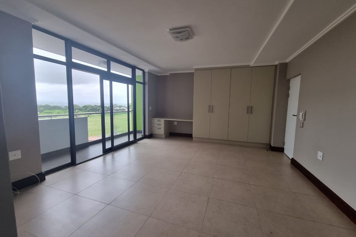Spacious bedroom featuring neutral tiled flooring, extensive built-in cupboards, a dedicated built-in desk, and large sliding glass doors leading to a balcony.