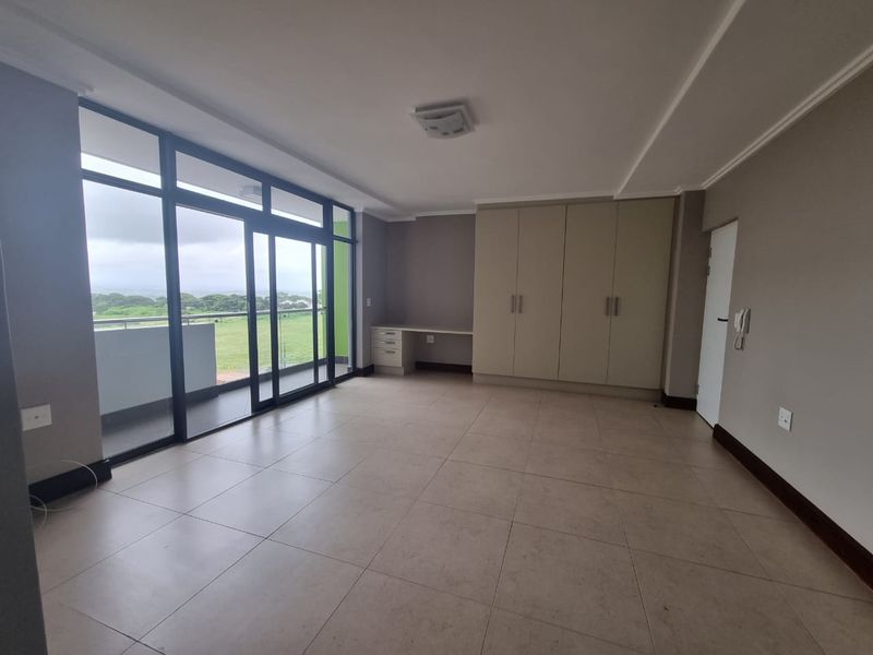 Spacious bedroom featuring neutral tiled flooring, extensive built-in cupboards, a dedicated built-in desk, and large sliding glass doors leading to a balcony.