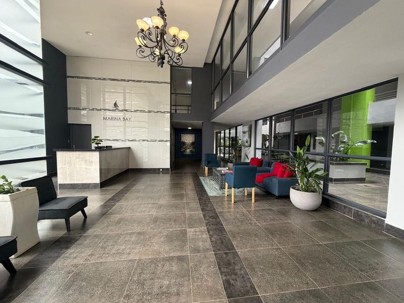 Spacious modern apartment building lobby featuring a reception desk, high ceilings, large glass windows, and contemporary tiled flooring.