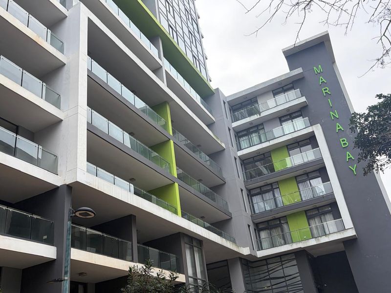 Exterior view of the Marina Bay apartment complex featuring modern architecture with glass-fronted balconies and a contemporary grey and green facade.