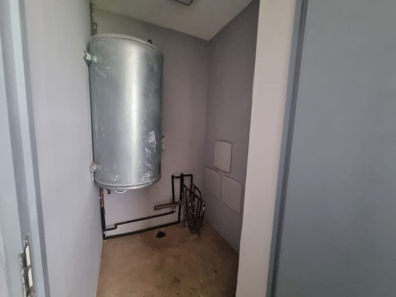 A small utility space featuring an exposed electric water heater and visible plumbing infrastructure.