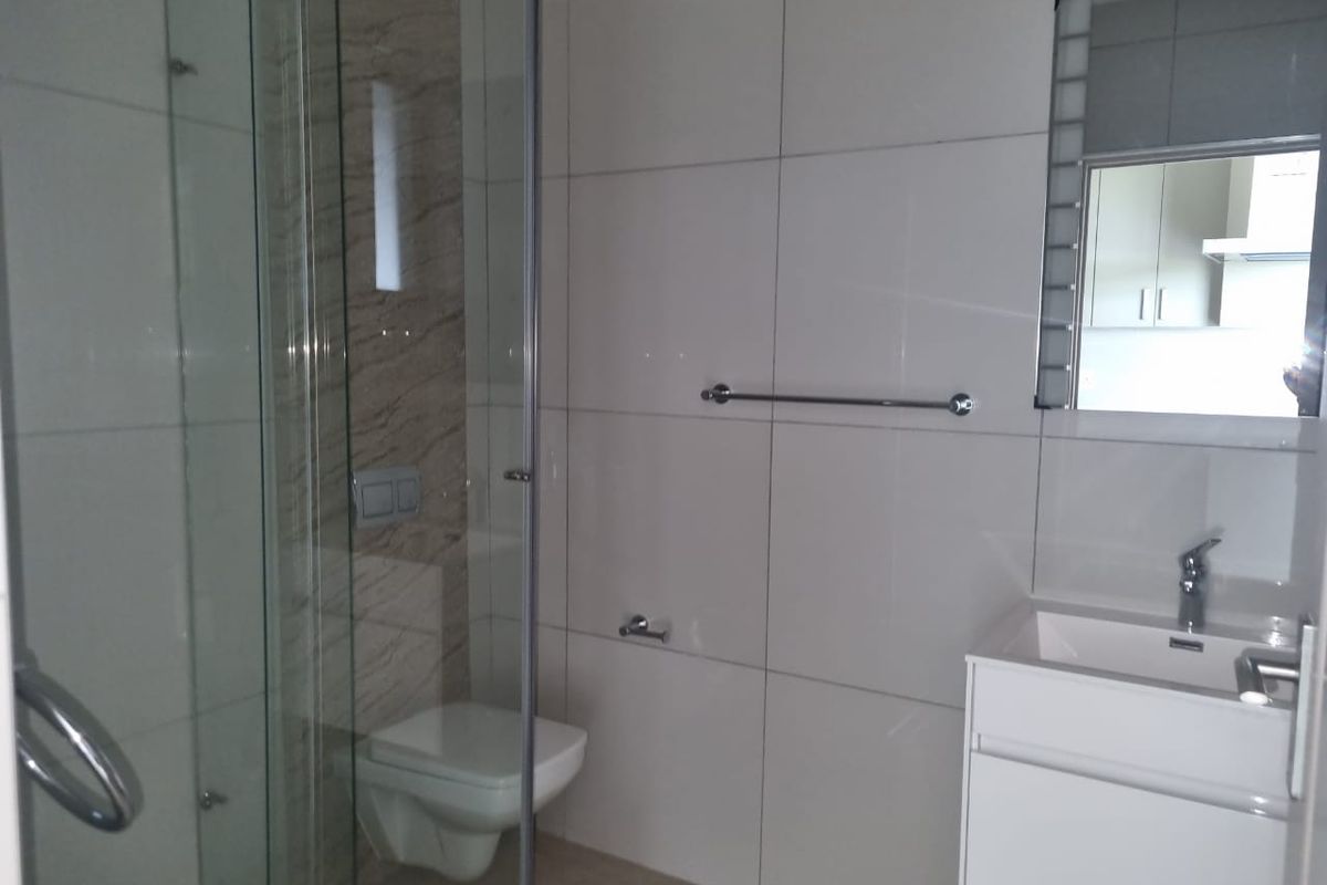 Modern bathroom featuring a glass-enclosed shower, wall-mounted toilet, and a sleek vanity basin with a mirror.
