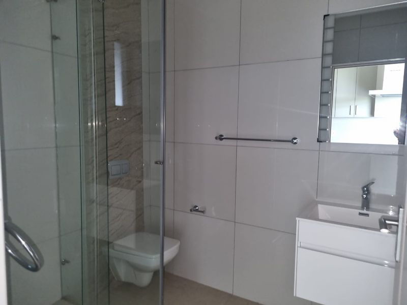 Modern bathroom featuring a glass-enclosed shower, wall-mounted toilet, and a sleek vanity basin with a mirror.