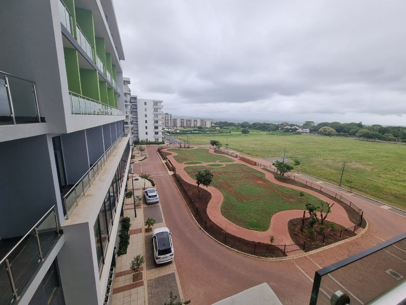 Elevated view overlooking the apartment complex grounds, featuring landscaped garden areas, paved pathways, and surrounding neighborhood landscape.