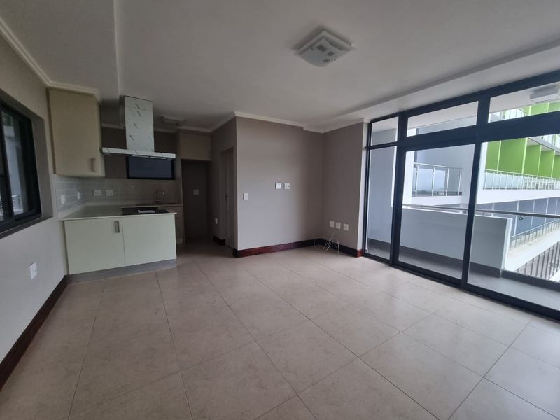 An open-plan living and kitchen area featuring tiled floors, modern cabinetry, and large sliding glass doors leading to a balcony.