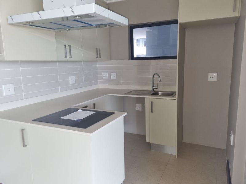 Modern kitchen featuring sleek built-in cabinetry, stone countertops, a stainless steel sink, and an integrated electric hob with an overhead extractor fan.