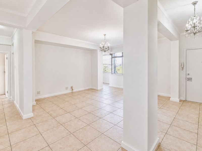 Spacious open-plan living area featuring neutral ceramic floor tiles, decorative crystal chandeliers, and clean white finishes throughout.