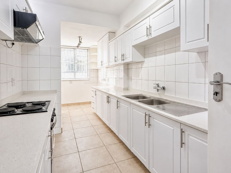 A clean, well-maintained kitchen featuring white cabinetry, stone countertops, a double basin sink, and a built-in electric hob with an extractor fan.