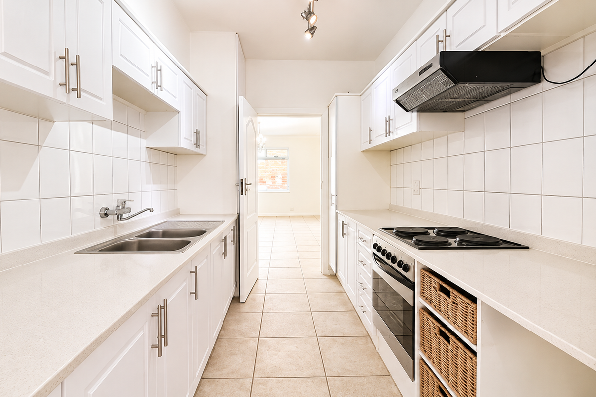 A clean, galley-style kitchen featuring white cabinetry, stone countertops, integrated oven and hob, and tiled finishes throughout.